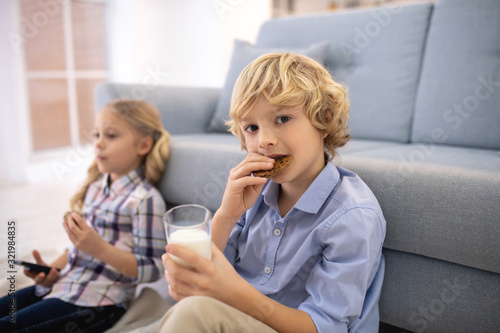 Boy biting off biscuit and drinking milk, girl switching channels