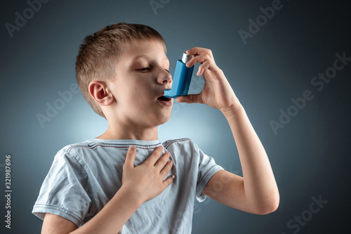 Portrait of a boy using an asthma inhaler to treat inflammatory diseases, shortness of breath. The concept of treatment for cough, allergies, respiratory tract disease. photo