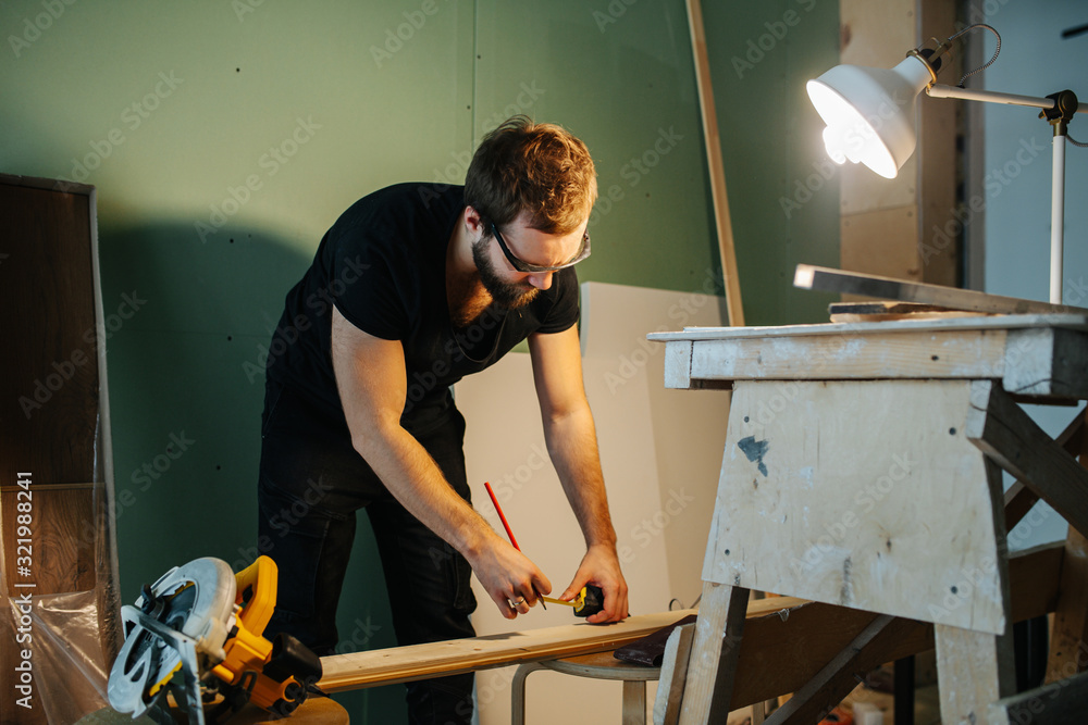 Man working on renovating his apartment. Measuring plank with a tape meter. Man working on renovating his apartment. Measuring plank with a tape meter.