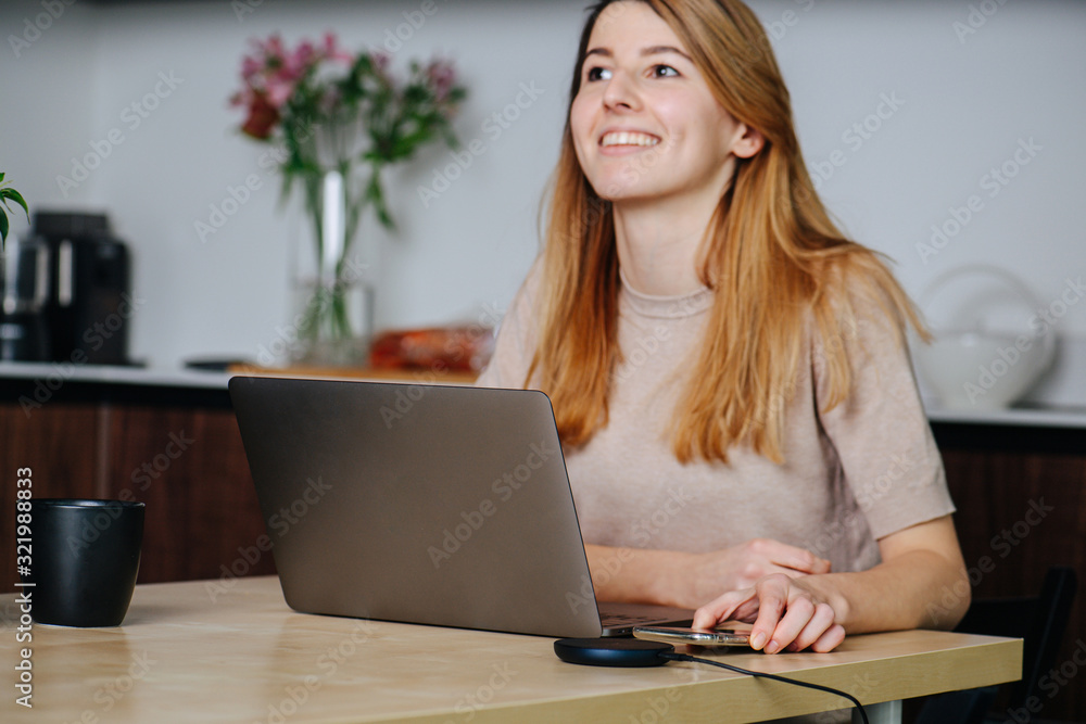 Happy woman working at the dining table, reaching for a phone on a pad Happy woman working at the dining table, reaching for a phone on a pad