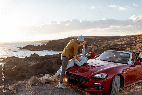 Young lovely couple kissing on the beach, traveling by car on the rocky ocean coast on a sunset. Carefree lifestyle, love and travel concept