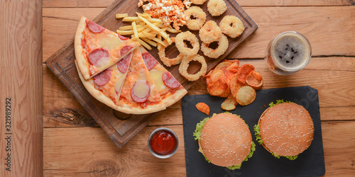 Fast food concept with greasy fried onion rings, burgers, and pizza with french fries and popcorn. Junk food concept.