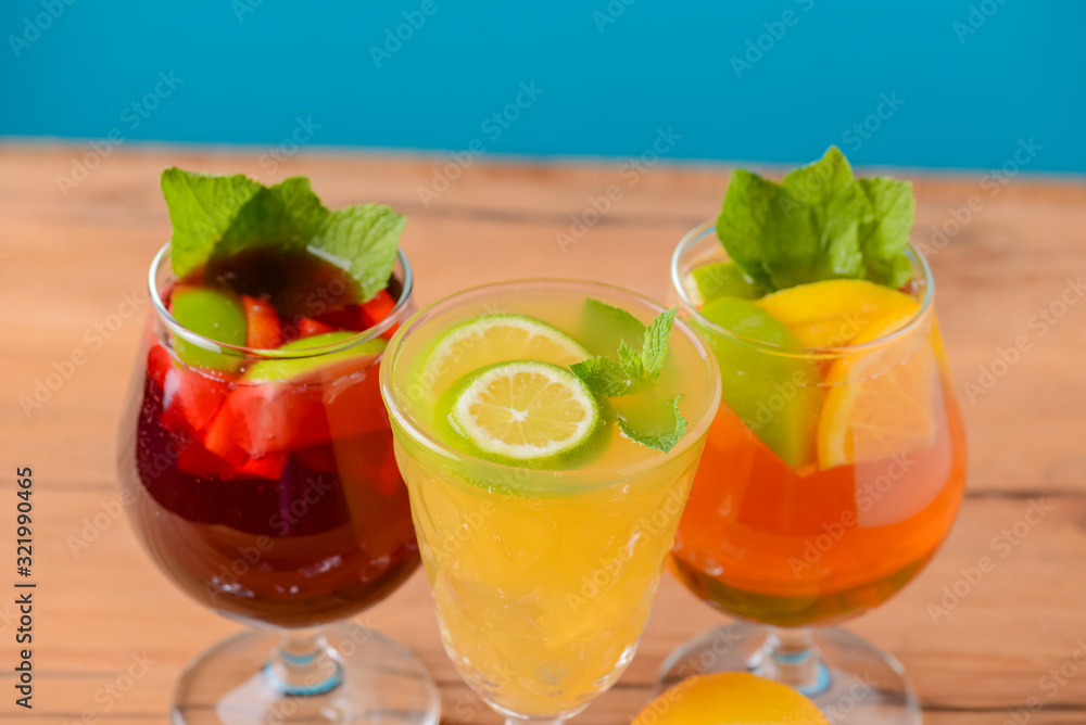 Three tropical mixed drinks with lime and lemon and mint leaves served in different glasses on rustic wooden table.