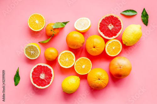Fresh citrus background. Oranges, grapefruits, leaves - whole fruits and halfs - on pink background top-down