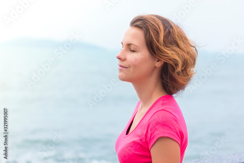 Beautiful girl enjoying walking at good summer sunny weather. Young woman breathing deep, deeply fresh sea air, smiling with eyes closed. Life is good. Relaxed lady dreaming. Calm, meditation concept © Евгений Шемякин