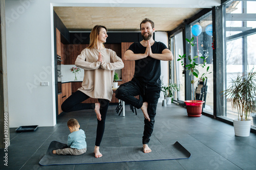 Parents standing in vrksasana position while their child plays next to them