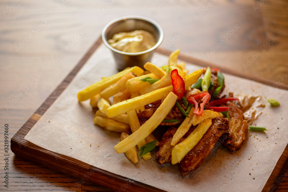 French Fries with fried chicken served with sauce on a wooden cutting board over wooden table background French Fries with fried chicken served with sauce on a wooden cutting board over wooden table background