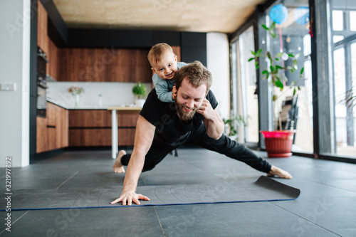 Father working out, doing single arm plank with his jolly baby riding on him