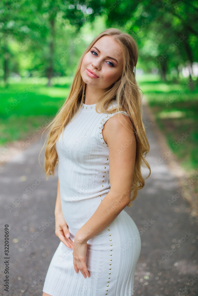 Portrait of a charming blond woman wearing beautiful white dress standing on the road under trees. Portrait of a charming blond woman wearing beautiful white dress standing on the road under trees.