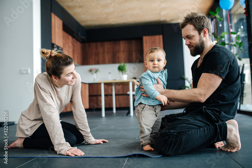 Young parents sitting on a yoga mat, spending time with their infant baby photo