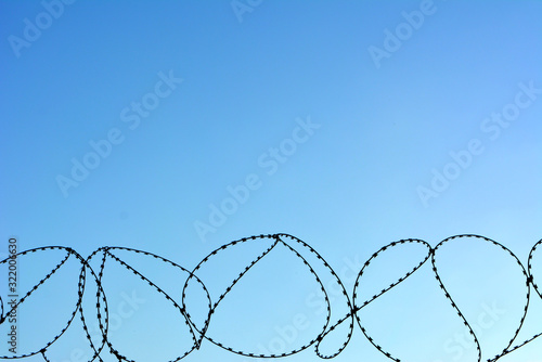 Barbed wire against the blue sky. The symbol of the forbidden  prison  protection  fencing  bondage. Texture. Wallpaper.