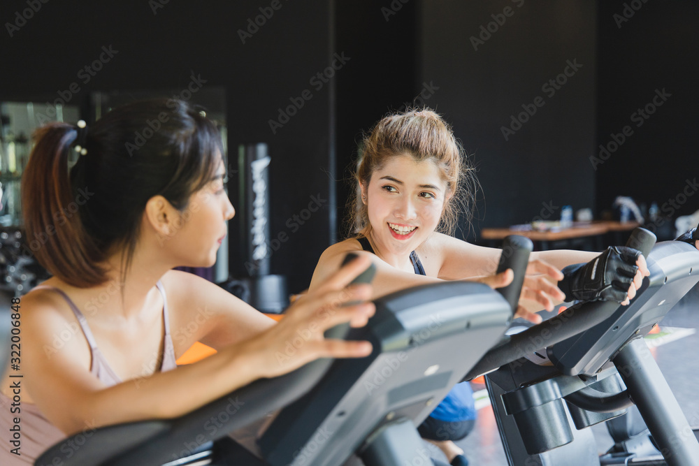 Fototapeta premium Asian Young woman beautiful people talking and smiling while working out on bike at gym.