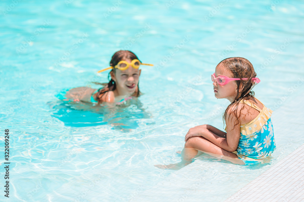 Adorable little girls playing in outdoor swimming pool on vacation