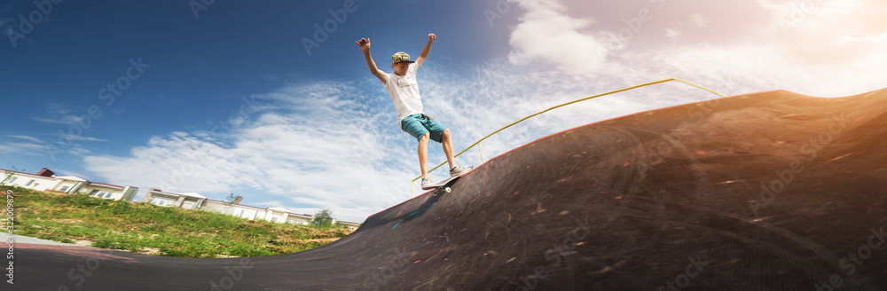 Fototapeta premium Portrait of a young skateboarder doing a trick on his skateboard on a halfpipe ramp in a skate park in the summer on a sunny day. The concept of youth culture of leisure and sports