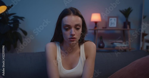 Millennial woman crying and washing off makeup while sitting on sofa at home. Depressed sad girl with messy mascara on her face worrying painfull broke up with boyfriend.