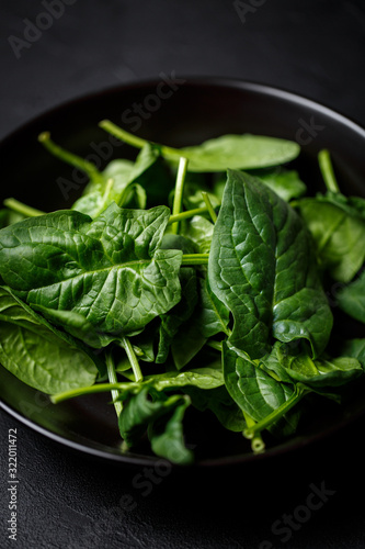 fresh spinach leaves in black plate on a dark background. top view