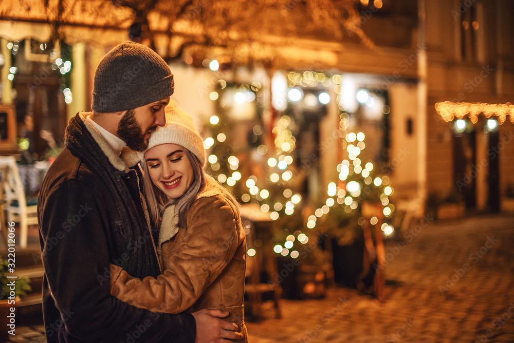 Outdoor night portrait of young happy hugging couple posing in street of European city. Copy, empty space for text