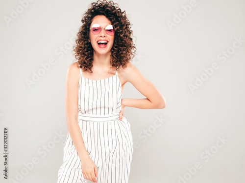 Portrait of beautiful smiling model with afro curls hairstyle dressed in summer hipster clothes.Sexy carefree girl posing in studio on gray background.Trendy funny and positive woman