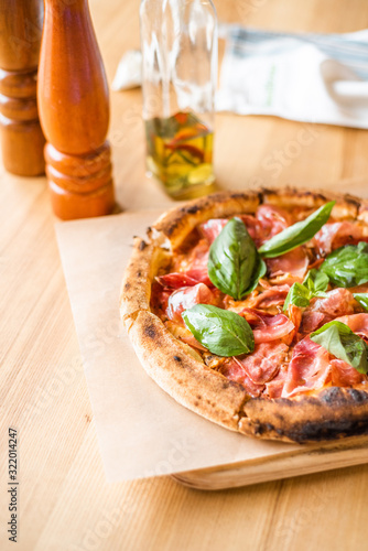 Delicious pizza stands on the table, pizza with red sauce, pancetta and basil, Italian cuisine, pizzeria