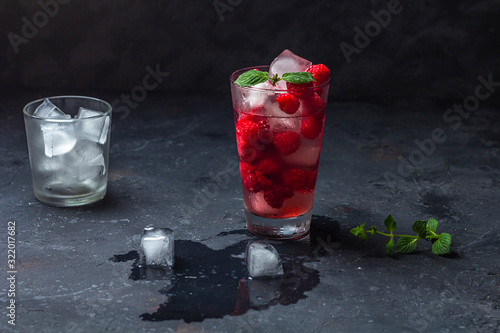 Raspberry alcoholic cocktail with liqueur, vodka, ice and mint on a dark background. Raspberry Mojito. Refreshing cool drink, lemonade or ice tea in a glass. Close up, copy space for text, low key