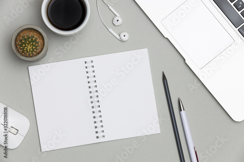 Blank notepad over laptop and headphones on gray office table