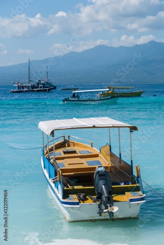 Barco fuera borda fondeando en un mar de azul cristalino con montañas y otros barcos al fondo photo