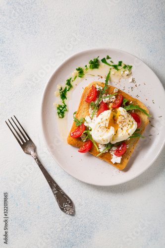 French breakfast concept. Poached egg on toasted bread with cherry tomatoes, cheese and herbs on a boiled background