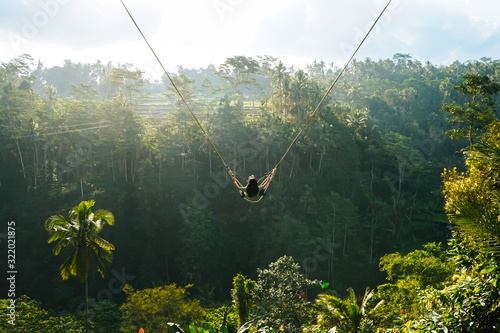 Back view of woman while swing with natural forest background in sunlight, travel and amazing concept.