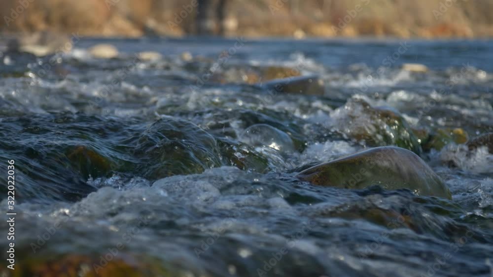 Low angle slow motion slider moving left to right over mossy small river rapids at Sunset/Golden Hour. River in shadows, background river bank kissed in sunshine. Low angle slow motion slider moving left to right over mossy small river rapids at Sunset/Golden Hour. River in shadows, background river bank kissed in sunshine.