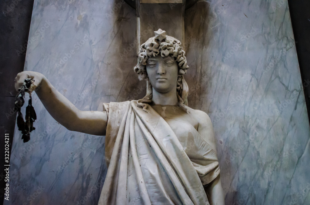 Una donna con una corona in mano su una tomba del cimitero monumentale di Bologna Una donna con una corona in mano su una tomba del cimitero monumentale di Bologna