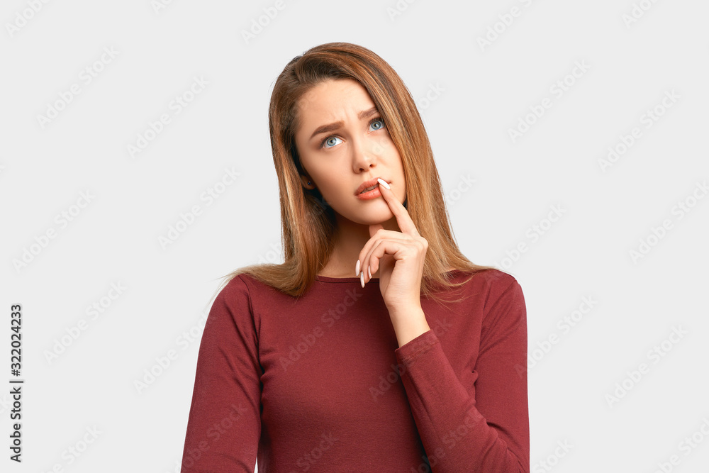 Photo girl looks with interest expression aside, keeps hand near lips. Beautiful young woman wears jacket sleeves isolated on white background in Studio with an empty space for text and advertising. Photo girl looks with interest expression aside, keeps hand near lips. Beautiful young woman wears jacket sleeves isolated on white background in Studio with an empty space for text and advertising.