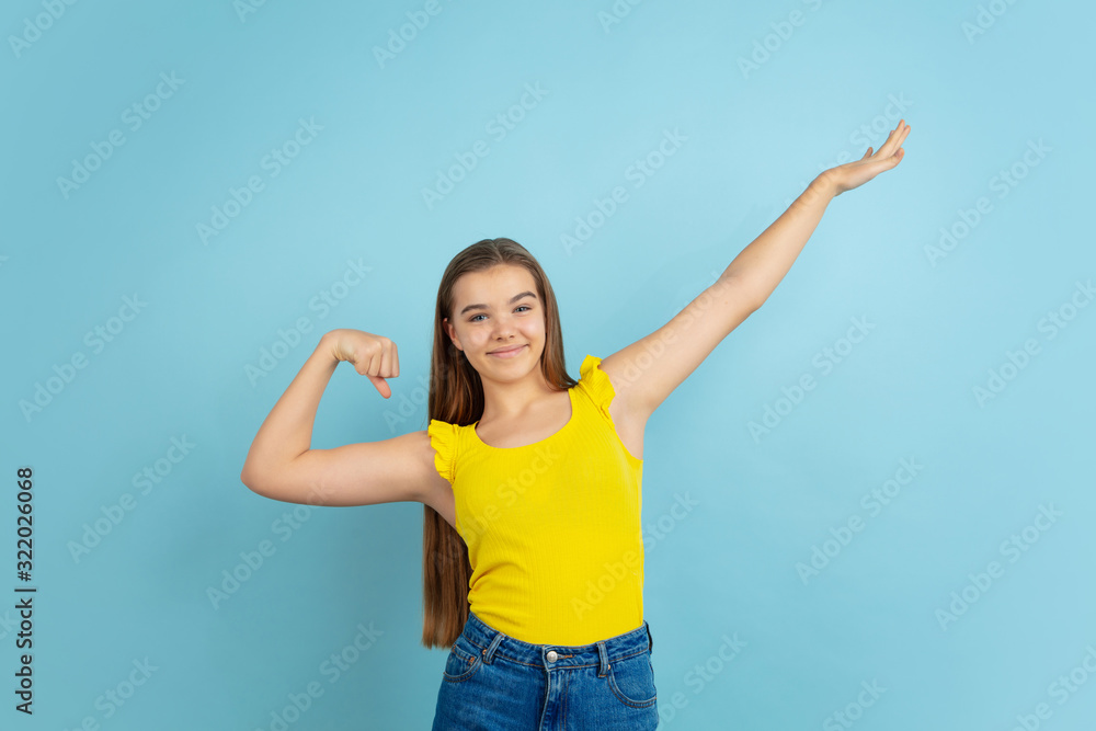 Successful winner. Caucasian teen girl's portrait isolated on blue background. Beautiful model in casual yellow wear. Concept of human emotions, facial expression, sales, ad. Copyspace. Looks cute. Successful winner. Caucasian teen girl's portrait isolated on blue background. Beautiful model in casual yellow wear. Concept of human emotions, facial expression, sales, ad. Copyspace. Looks cute.