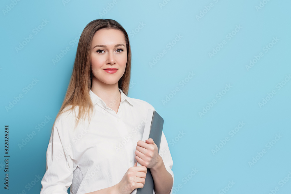 A young student girl in a white shirt holds a folder in her hands on a blue background with copy space for text. Cute student with documents, papers in hands. Business woman in office clothes