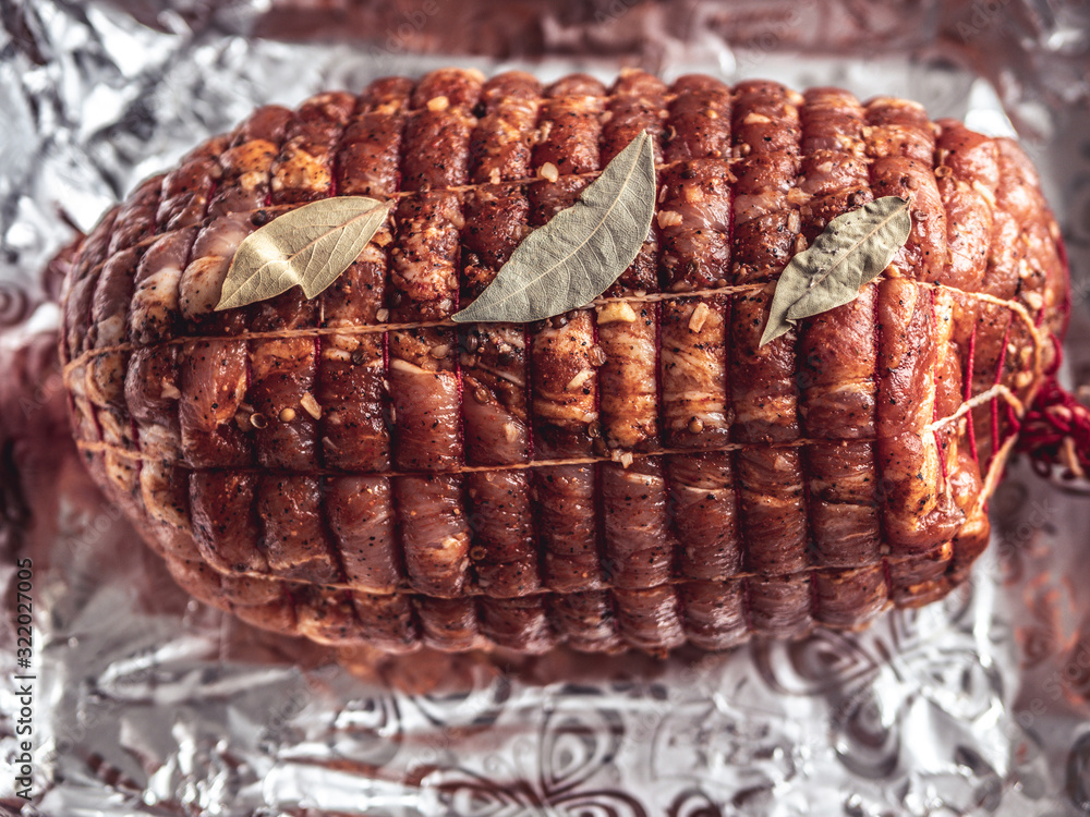 Obraz premium Baking tray with raw turkey meatloaf on table. Uncooked spicy pork meat roulade prepared to roast, marinated with spices and herbs on black slate plate, view from above, close-up