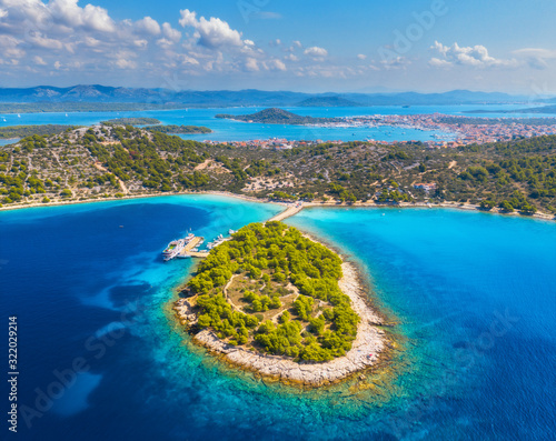 Fototapeta Naklejka Na Ścianę i Meble -  Aerial view of beutiful small island in sea bay at sunny day in summer in Murter, Croatia. Top view of transparent blue water, green trees, mountain, sandy beach, boats and yachts. Tropical landscape