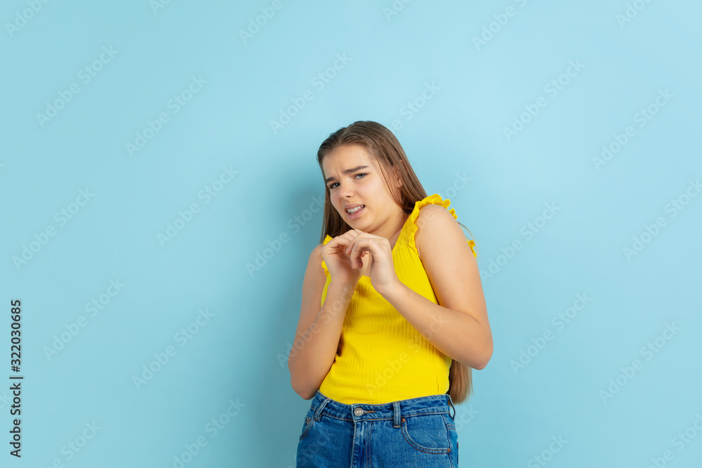 Shocked, scared. Caucasian teen girl's portrait isolated on blue background. Beautiful model in casual yellow wear. Concept of human emotions, facial expression, sales, ad. Copyspace. Looks cute. Shocked, scared. Caucasian teen girl's portrait isolated on blue background. Beautiful model in casual yellow wear. Concept of human emotions, facial expression, sales, ad. Copyspace. Looks cute.