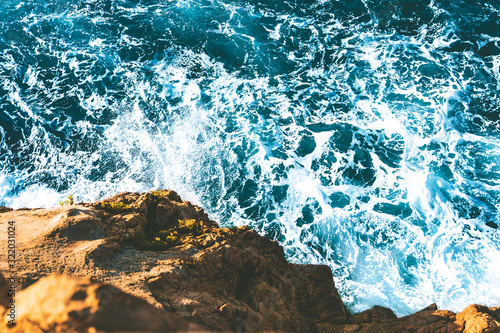 top view of sea waves hitting rocks on the beach with turquoise blue sea water. rock cliff seascape in Atlantic ocean coastline. splashing water in coast with rocks with spray and foam.