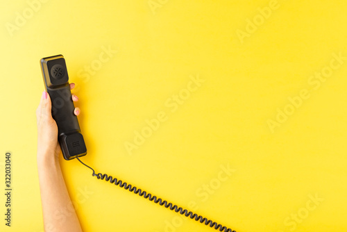 Woman’s hand holding vintage handset on yellow background. Customer support concept