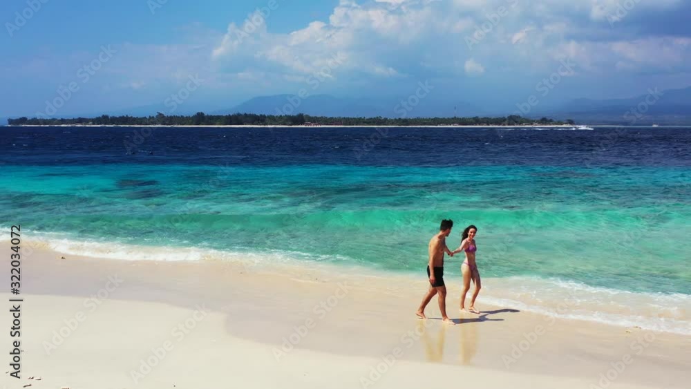Young couple walking on sandy beach alongside blue turquoise sea with white waves on a cloudy windy day in Indonesia Young couple walking on sandy beach alongside blue turquoise sea with white waves on a cloudy windy day in Indonesia