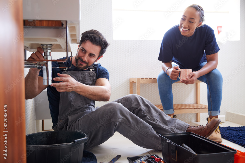 Male Plumber Teaching Female Apprentice To Fix Leaking Sink In Home Bathroom Male Plumber Teaching Female Apprentice To Fix Leaking Sink In Home Bathroom