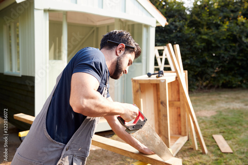 Fotografie Male Carpenter With Female Apprentice Sawing Wood To Build Outdoor Summerhouse I