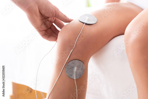 Cropped view of therapist setting electrodes on knee of patient on massage couch on white background photo
