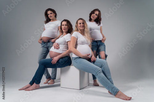 Four pregnant girls in white t-shirts and jeans.