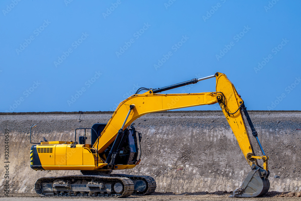 The big yellow backhoe is working on the ground at the outdoor construction project with the blue sky background in the sunny day. The big yellow backhoe is working on the ground at the outdoor construction project with the blue sky background in the sunny day.