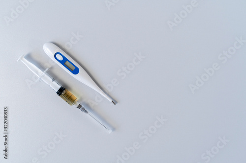 Electronic thermometer and syringe with medicine on a gray background. An injection from temperature. Medical concept.