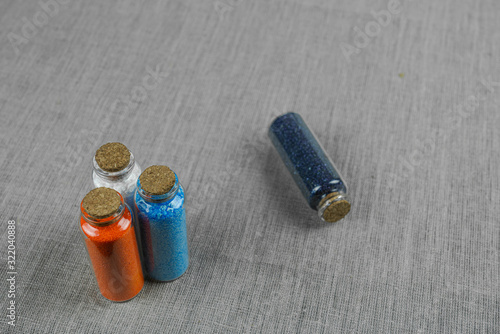 Blue, red, white and indigo powder and crystalls crystals in small bottles on gray linen background