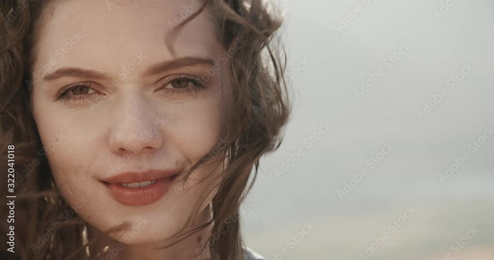 Brunette caucasian girl looking at camera and smiling as wind blows her hair in mountains - freedom concept close up portrait 4k footage Brunette caucasian girl looking at camera and smiling as wind blows her hair in mountains - freedom concept close up portrait 4k footage