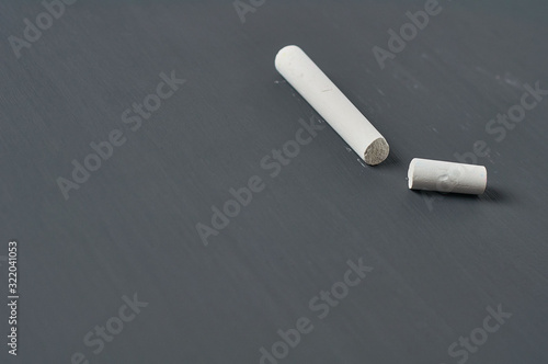 One white broken piece of chalk on black chalkboard. Copy space