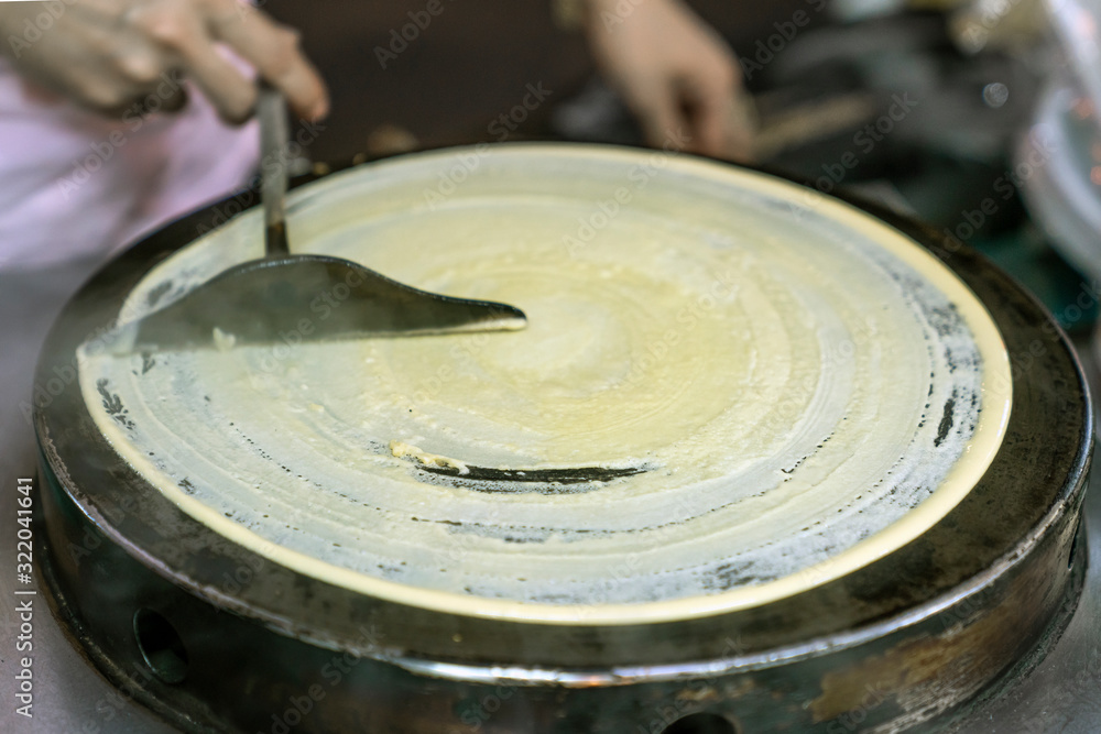 Cooking Thai pancakes: the cook rolls the dough with a spatula on a hot pancake pan. Traditional street food in Thailand