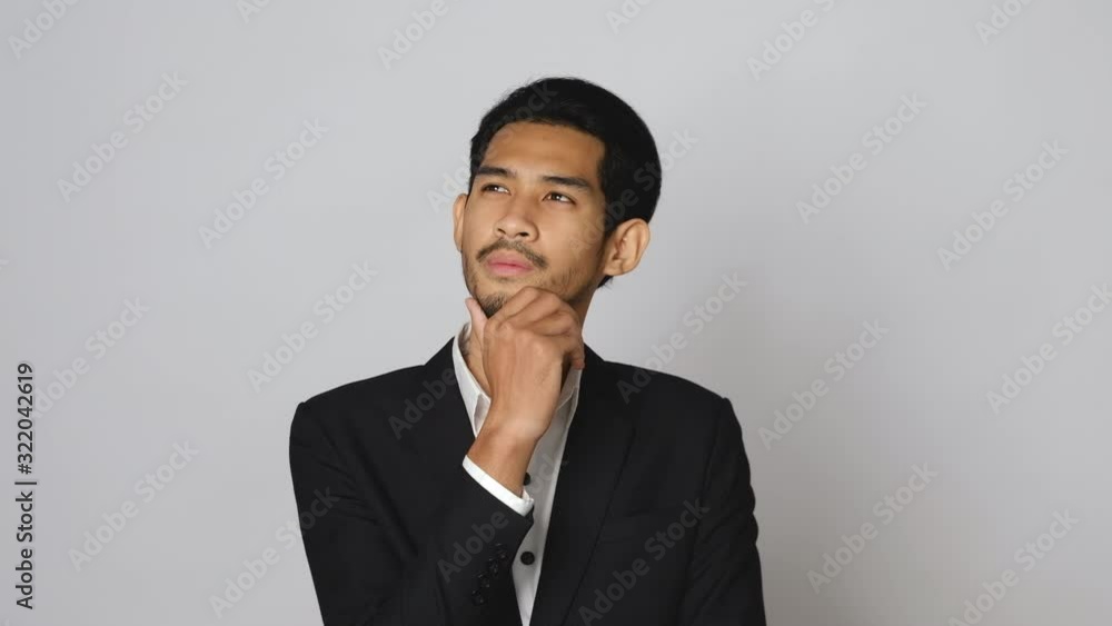 Thoughtful young asian businessman holding hand on chin over gray background, thinking and having idea. Thoughtful young asian businessman holding hand on chin over gray background, thinking and having idea.